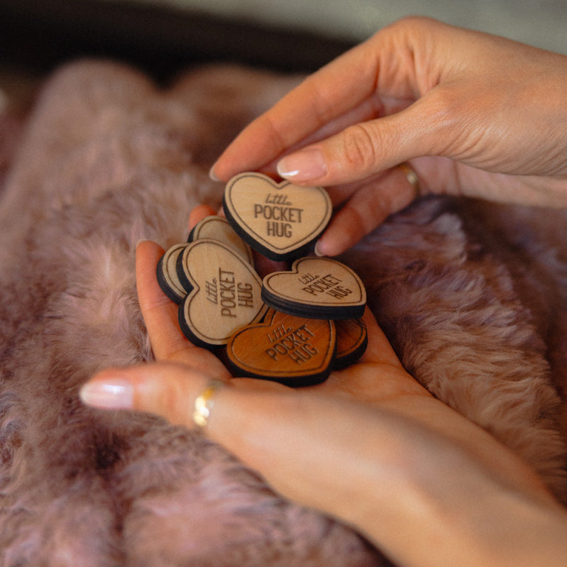Heart-shaped wooden little pocket hugs held by a hand in front of a fireplace