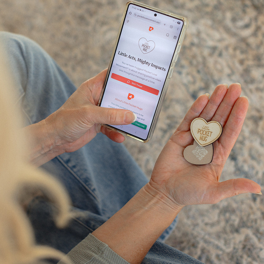 Person holding a smartphone with an app open and a heart-shaped little pocket hug in their other hand.